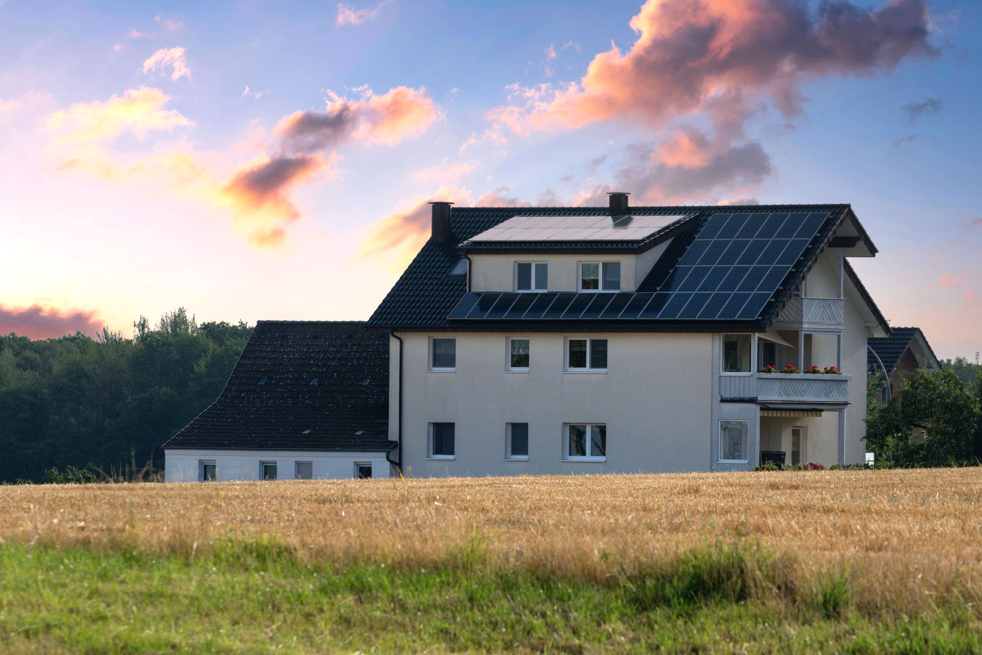 Wohnhaus mit Solarkollektoren auf dem Dach am Abend, davor eine Wiese